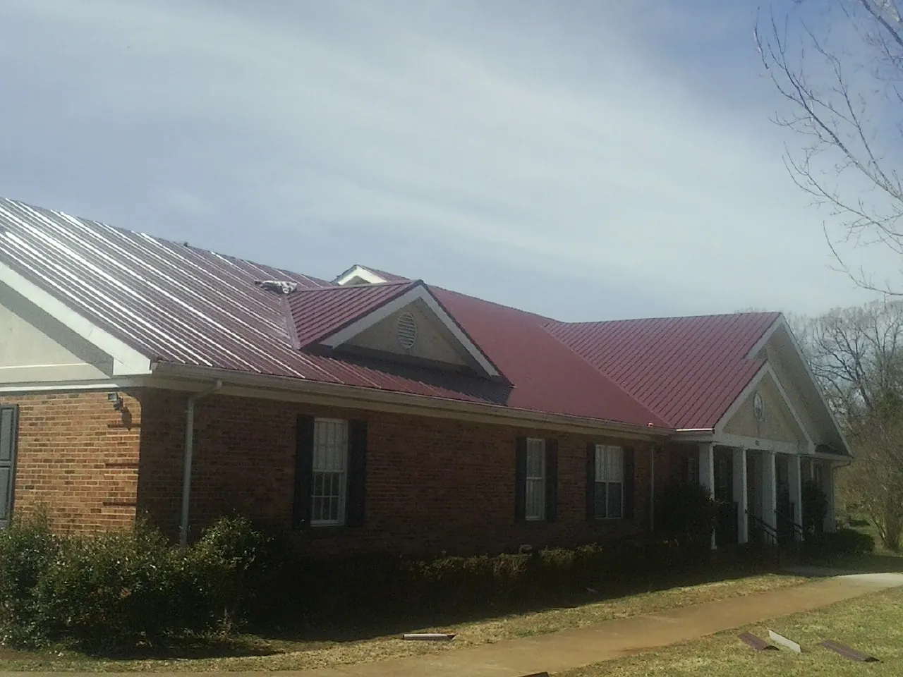 Red metal roof with gabled entries on a long brick building, from a Hail Damage Roof Repair job in Skamokawa