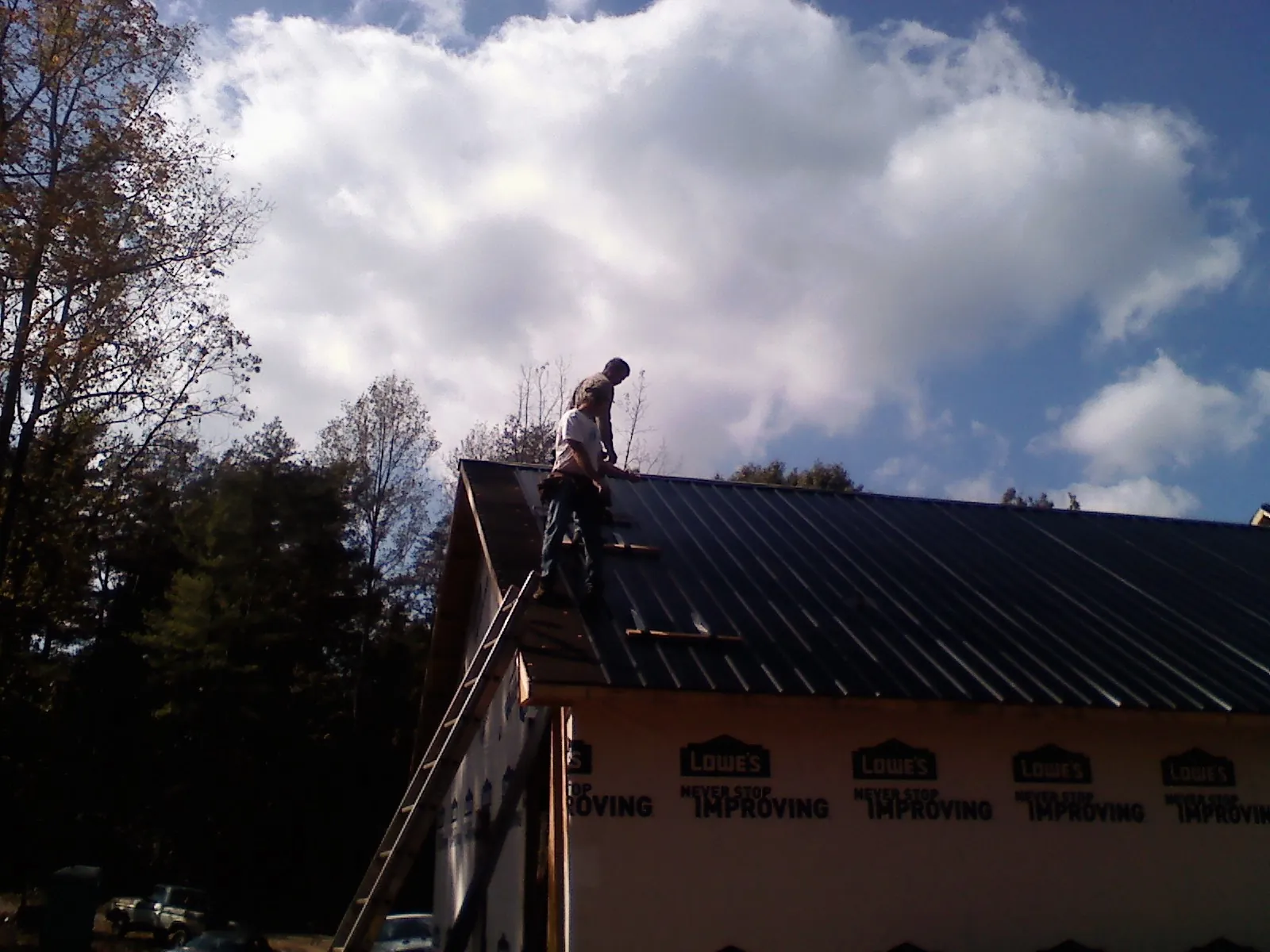 Roofer fastening dark metal panels high against a cloudy sky, from a Roof Inspection job in Skamokawa