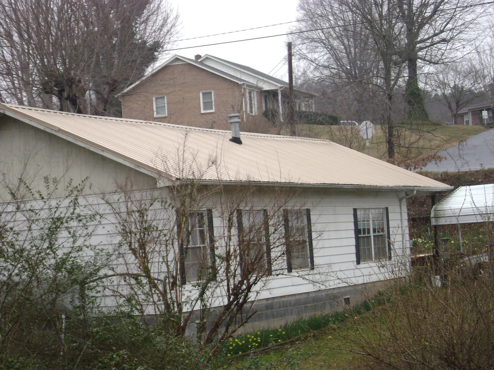 Tan metal roof on a white sided house set into a hillside — Commercial Roofing by Roofing Brothers in Skamokawa